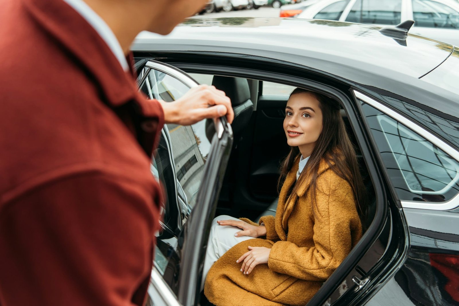 Over shoulder view of taxi driver opening car door for woman